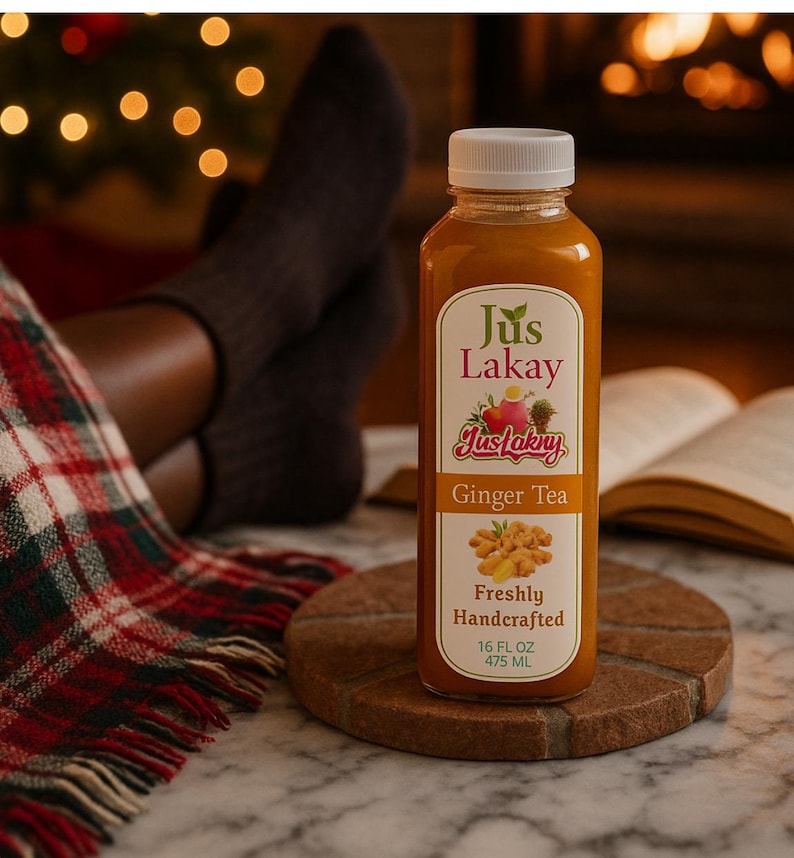 Peut inclure: Une bouteille transparente de Jus Lakay Ginger Tea avec un bouchon blanc, pos&eacute;e sur un dessous de verre en bois. L'&eacute;tiquette pr&eacute;sente du texte et des illustrations de gingembre et de fruits. La bouteille contient 475 ml de th&eacute;.