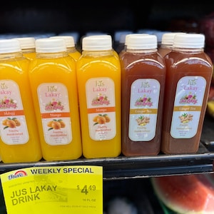 Peut inclure: Plusieurs bouteilles de Jus Lakay, saveurs mangue et th&eacute; au gingembre. Le jus de mangue est jaune vif, tandis que le th&eacute; au gingembre est brun rouge&acirc;tre. Chaque bouteille a un bouchon blanc et une &eacute;tiquette avec le nom de la marque et des illustrations de fruits.