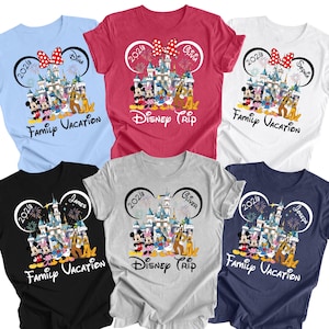 Peut inclure: Une collection de six t-shirts en bleu clair, rouge, blanc, noir, gris et bleu marine. Chaque t-shirt présente un motif de château, de feux d'artifice et de personnages de dessins animés encadrés par des oreilles de souris avec le texte 2026.
