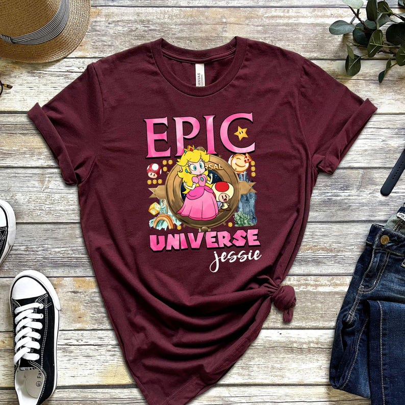 May include: Burgundy t-shirt featuring a cartoon graphic of Princess Peach from the Super Mario video game series. The design includes the word "EPIC" in pink, and the words "UNIVERSE Jessie".