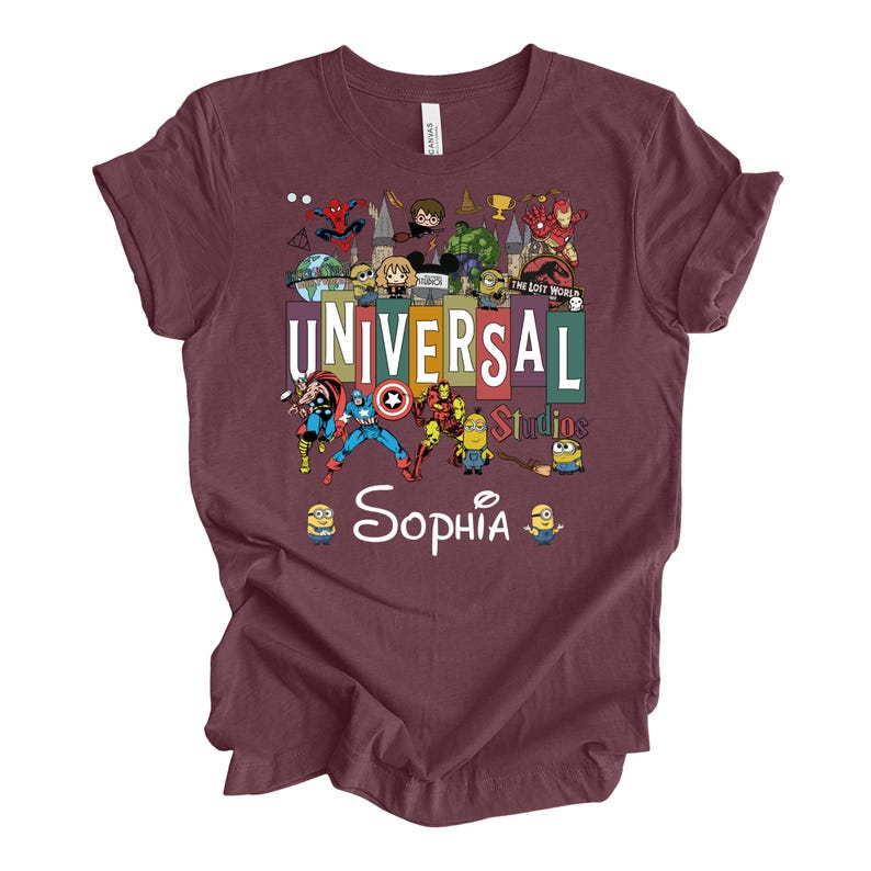 Op de afbeelding: Bordeaux t-shirt met een kleurrijke afbeelding van Universal Studios-personages, waaronder Spider-Man, Minions en superhelden. De tekst "UNIVERSAL Studios" staat prominent afgebeeld, met de naam "Sophia" eronder. Een leuke, thematische tee.
