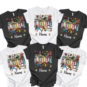 Op de afbeelding: Een verzameling zwarte en witte t-shirts, elk met een kleurrijk grafisch ontwerp. Het ontwerp bevat de tekst "UNIVERSAL Studios" en "NAME", samen met verschillende stripfiguren. De shirts zijn korte mouwen.