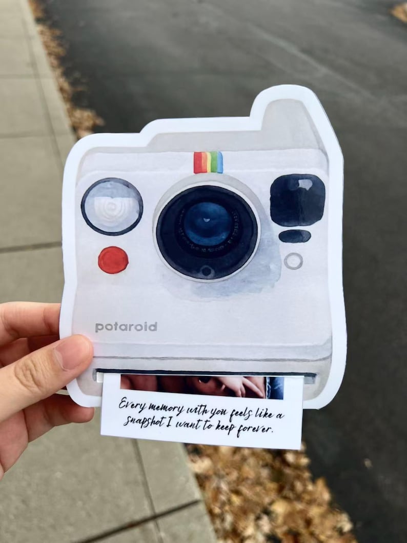 May include: A white Polaroid camera-shaped sticker with a rainbow stripe and the word "potaroid". The sticker has a photo print that reads "Every memory with you feels like a snapshot I want to keep forever."
