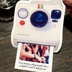 May include: White Polaroid-style sticker with a watercolor design. The sticker features a blue lens, a red button, and a rainbow stripe. A photo is printed at the bottom with the text: "Every memory with you feels like a snapshot I want to keep forever."