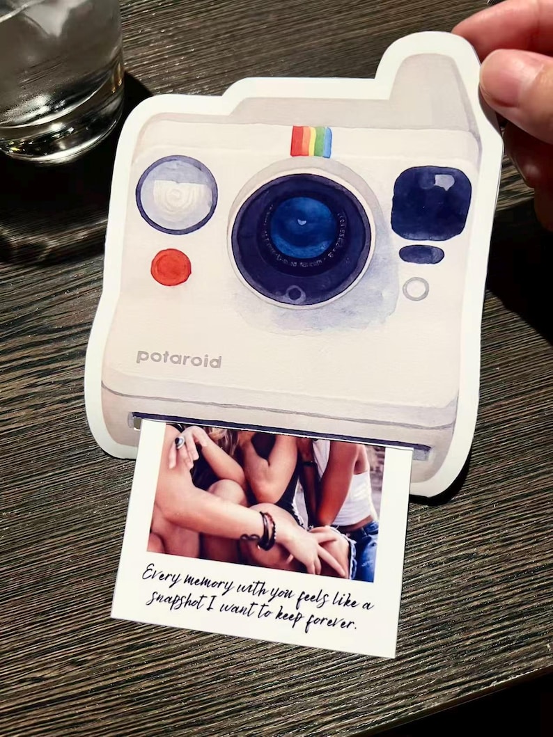 May include: White Polaroid-style sticker with a watercolor design. The sticker features a blue lens, a red button, and a rainbow stripe. A photo is printed at the bottom with the text: "Every memory with you feels like a snapshot I want to keep forever."