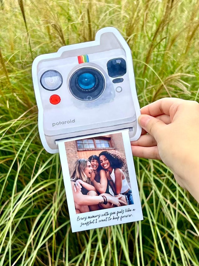May include: A white Polaroid-style photo holder with a rainbow stripe detail and the word "potaroid" printed on the front. The holder displays a photo of three smiling people. The photo has the text: "Every memory with you feels like a snapshot I want to keep forever."