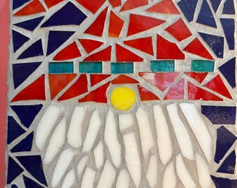 Op de afbeelding: Een mozaïekkunstwerk met een gestileerd ontwerp. Het mozaïek maakt gebruik van rode, blauwe, witte, gele en turquoise glazen stukken. Het ontwerp omvat een rood en blauw bovendeel, een gele cirkel en witte, baardachtige vormen aan de onderkant.