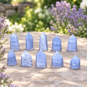 May include: A collection of ten light blue lace agate crystal towers arranged in two rows. Each stone features a pointed top and a polished surface with distinct white and pale blue banding patterns, showcasing natural variations in colour and texture.