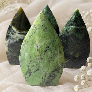 May include: Three polished stone sculptures shaped like teardrops or flames. The front piece is a vibrant lime green with dark grey veining, while the two pieces behind it are a deeper, darker forest green with mottled black and dark green patterns.
