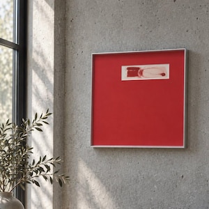 Pode incluir: Uma peça de arte de parede quadrada com um fundo vermelho vibrante e uma moldura prateada fina. Centrado na parte superior, há um pequeno encaixe retangular branco contendo um design abstrato de pinceladas vermelho-escuras e linhas finas.