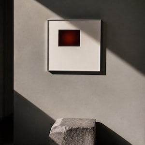 May include: A square wall-mounted frame featuring a wide white mat board and a thin metallic border. Centered within the mat is a rectangular aperture revealing a deep, dark red gradient that transitions into a black center point.