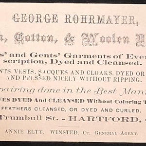 May include: A rectangular off-white business card with black printed text reading George Rohrmayer, Silk, Cotton, & Woolen Dyer, offering garment dyeing, cleaning, and repair services at No. 24 Trumbull St., Hartford, Conn., with Annie Elty as agent.