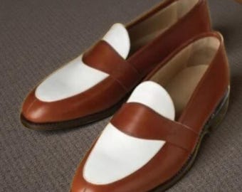 May include: A pair of brown and white leather loafers. The shoes have a classic design with a brown upper and a white vamp. The loafers are displayed on a neutral surface.