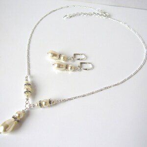 May include: A silver-toned necklace and matching pair of lever-back earrings. The necklace features a delicate chain with cream-colored teardrop and round pearls accented by small, clear rhinestones. The earrings mirror this pearl and rhinestone design.
