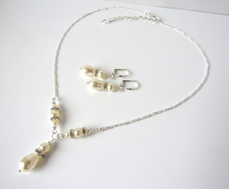 May include: A silver-toned necklace and matching pair of lever-back earrings. The necklace features a delicate chain with cream-colored teardrop and round pearls accented by small, clear rhinestones. The earrings mirror this pearl and rhinestone design.