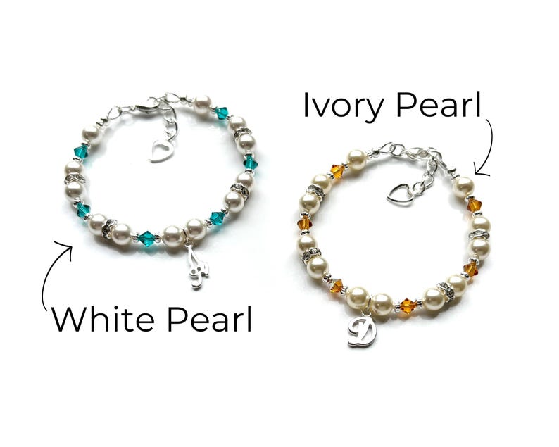 May include: Two pearl bracelets with charms. The bracelet on the left has white pearls and teal blue crystals with a music note charm. The bracelet on the right has ivory pearls and amber crystals with a letter D charm.  White Pearl and Ivory Pearl are written below the bracelets.