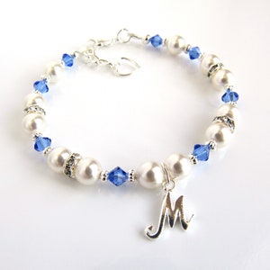 May include: A white pearl bracelet with blue crystal accents and a silver charm with the letter 'M'.