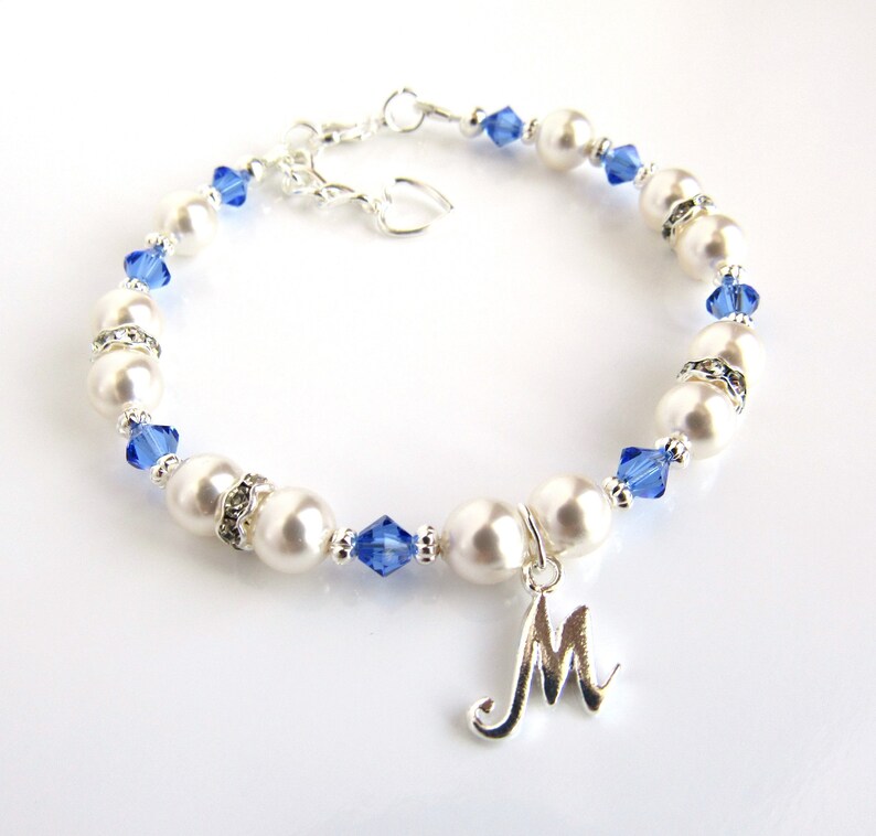 May include: A white pearl bracelet with blue crystal accents and a silver charm with the letter 'M'.