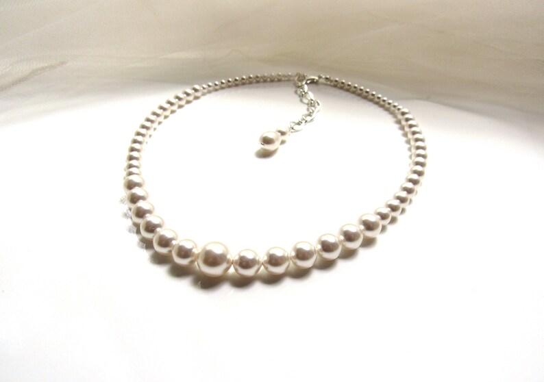 May include: A white pearl necklace with a silver clasp. The necklace is made of round pearls and is approximately 18 inches long.