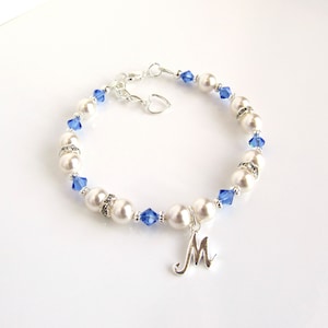 May include: A white pearl and blue crystal bracelet with a silver charm in the shape of the letter M.
