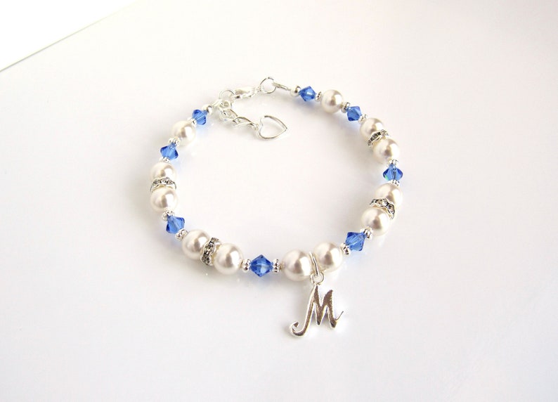 May include: A white pearl and blue crystal bracelet with a silver charm in the shape of the letter M.