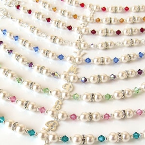 May include: A set of pearl bracelets with different colored crystal accents. Each bracelet features a silver charm with a letter.