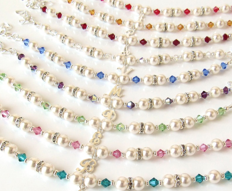 May include: A set of pearl bracelets with different colored crystal accents. Each bracelet features a silver charm with a letter.