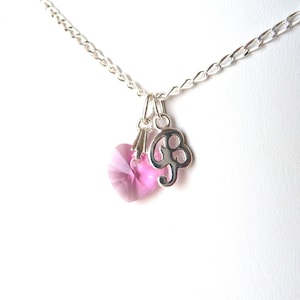 May include: A silver chain necklace with a pink crystal heart and a silver charm with the letter 'G'.
