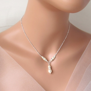 May include: A silver-toned necklace featuring a delicate chain with small clear crystals and a central drop pendant. The pendant consists of a single cream-colored teardrop-shaped pearl accented by a small clear crystal spacer above it.