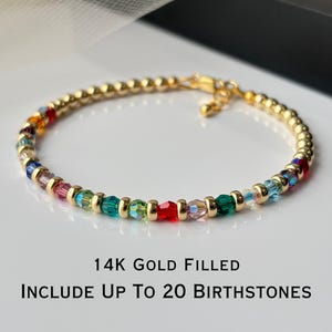 May include: Gold-filled bracelet with colorful birthstones. The bracelet features a delicate chain with small, gold beads and a variety of colorful gemstones. The text on the image reads: "14K Gold Filled, Include Up To 20 Birthstones."