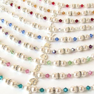 May include: A collection of pearl bracelets with crystal accents in various colors. Each bracelet features a silver charm with a letter.