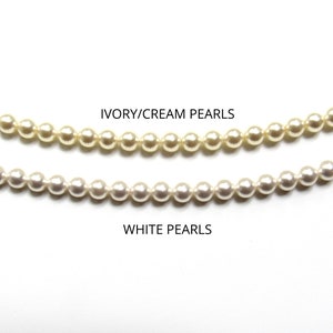 May include: Two strands of pearls, one strand is ivory/cream colored and the other strand is white. The text "IVORY/CREAM PEARLS" is above the ivory/cream strand and the text "WHITE PEARLS" is below the white strand.