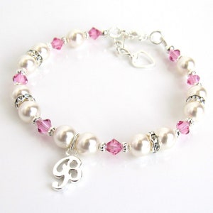 May include: A white pearl and pink crystal bracelet with a silver charm in the shape of the number 8. The bracelet has a silver heart charm and a lobster clasp.