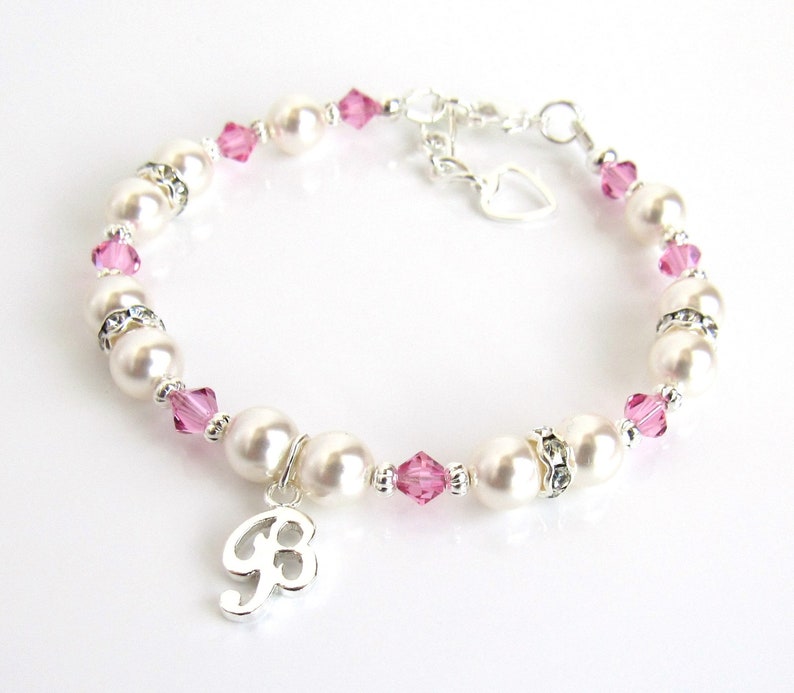 May include: A white pearl and pink crystal bracelet with a silver charm in the shape of the number 8. The bracelet has a silver heart charm and a lobster clasp.