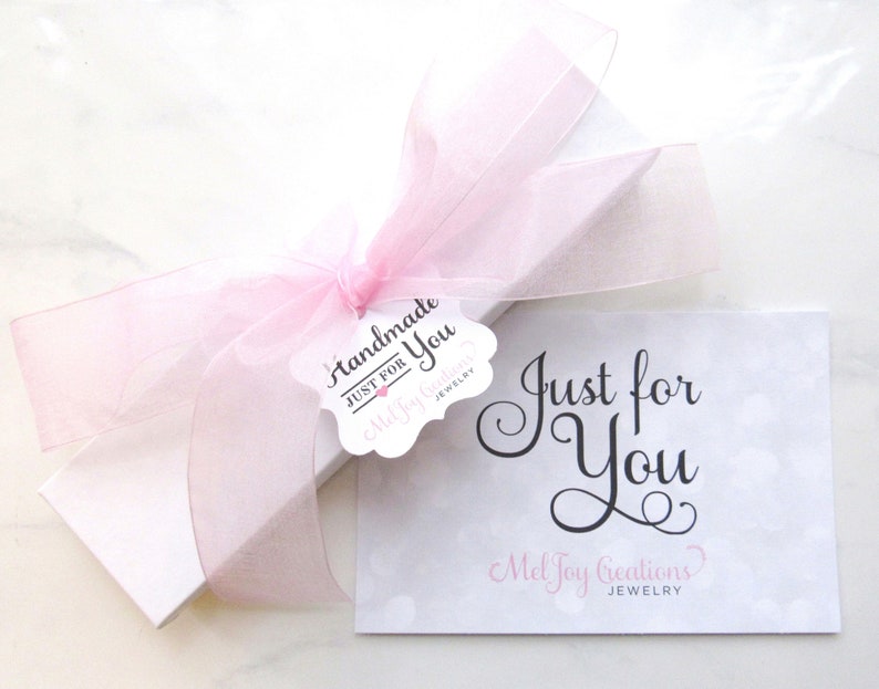 May include: A white gift box with a pink ribbon and a tag that says "Handmade Just for You Mel Joy Creations Jewelry". The box is sitting on a white surface with a card that says "Just for You Mel Joy Creations Jewelry".