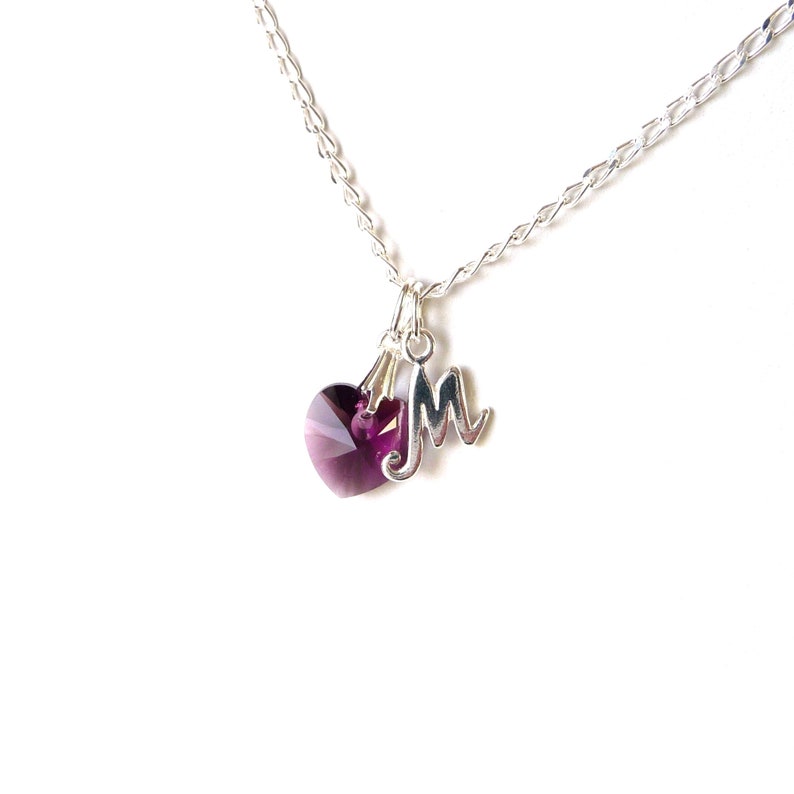 May include: A silver chain necklace with a purple heart charm and a silver letter 'M' charm.