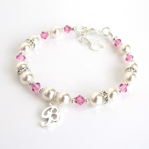 May include: A silver bracelet with pink crystals and white pearls. The bracelet has a silver charm with the letter "B" on it.