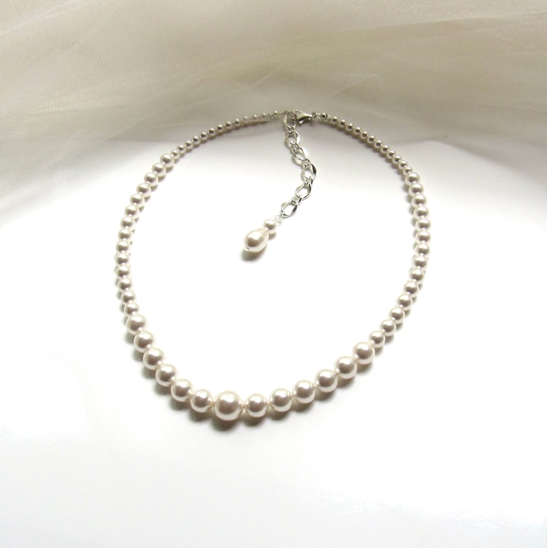 May include: A white pearl necklace with a silver clasp and a single pearl drop pendant.