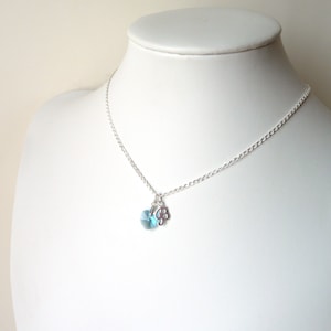 May include: A silver chain necklace with a light blue crystal and a silver flower charm.