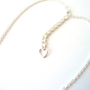 May include: A silver chain necklace with a heart-shaped clasp. The chain is made of small, linked circles.