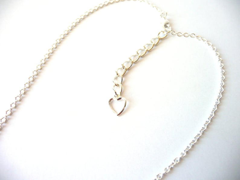 May include: A silver chain necklace with a heart-shaped clasp. The chain is made of small, linked circles.