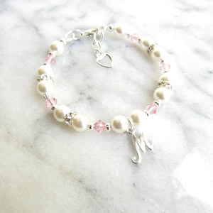 May include: A silver bracelet with white pearls, pink crystals, and a silver charm with the letter 'M'.