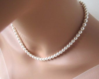 May include: A delicate pearl necklace with small, round, off-white pearls. The necklace is draped around a person's neck, showcasing its elegant design. The pearls are evenly spaced, creating a classic and timeless look.