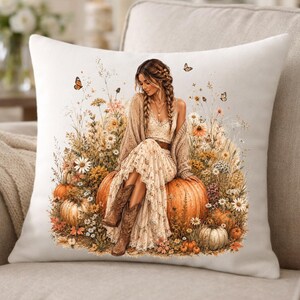 Puede incluir: Un cojín decorativo con una ilustración en acuarela de una mujer sentada sobre una calabaza. La mujer lleva un vestido floral y botas, rodeada de flores y mariposas. La paleta de colores incluye naranja, beige y marrón.