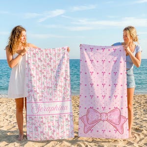 Puede incluir: Dos toallas de playa con diseños florales y de lazo. Una toalla presenta flores rosas y el nombre "Seraphina" en una pancarta. La otra toalla es de color rosa claro con un patrón de lazo y un lazo grande con el nombre "Seraphina".