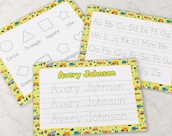 May include: Three rectangular educational tracing mats with a yellow border featuring construction vehicles and trees. One mat shows shapes with labels, one shows the alphabet in dotted lines, and one shows the name Avery Johnson in dotted lines.