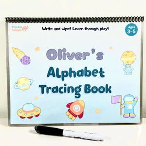 May include: A spiral-bound alphabet tracing book for children aged 3-5, with a light blue cover decorated with space-themed illustrations. The cover displays "Oliver's Alphabet Tracing Book" and "Write and wipe! Learn through play!" A black and white marker is in the foreground.