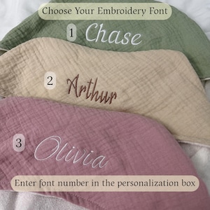 Peut inclure: Trois &eacute;chantillons de tissu mousseline superpos&eacute;s en vert sauge, beige et vieux rose. Chaque &eacute;chantillon pr&eacute;sente des pr&eacute;noms brod&eacute;s : 'Chase' en blanc, 'Arthur' en marron et 'Olivia' en blanc. Le texte indique : 'Choose Your Embroidery Font' et 'Enter font number in the personalization box'.