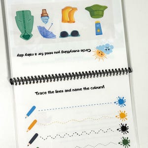 May include: A spiral-bound educational activity sheet featuring two sections. The top section shows illustrations of a green raincoat, ice cream, yellow boots, a green hat, a blue umbrella, sunglasses, and sunscreen with text prompts. The bottom section displays colored pencils and dashed lines leading to paint splatters with the text Trace the lines and name the colours!