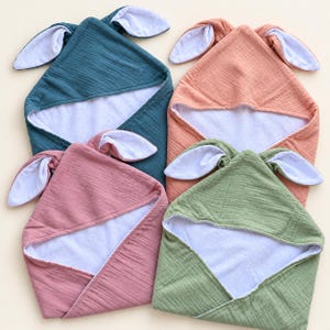 Peut inclure: Quatre couvertures &agrave; capuche en bleu sarcelle, p&ecirc;che, vieux rose et vert sauge. Chaque couverture pr&eacute;sente une capuche triangulaire avec deux longues oreilles de lapin doubl&eacute;es de blanc. Le tissu ext&eacute;rieur est froiss&eacute;, l'int&eacute;rieur est blanc.